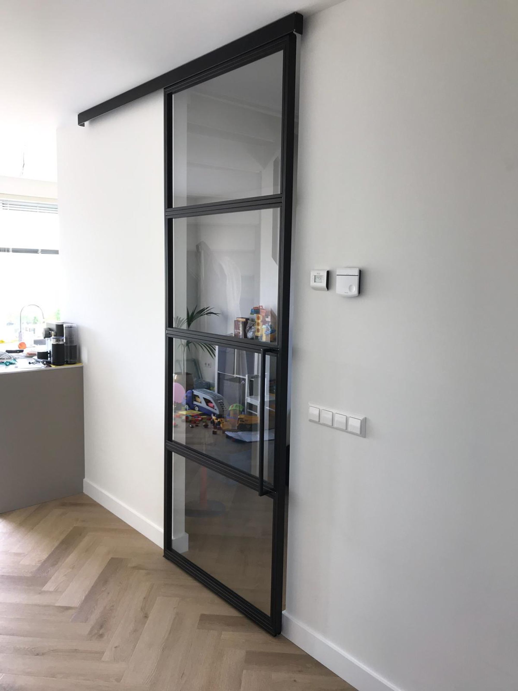 Stalen schuifdeur met softclose systeem rail prachtig  onder eikenvisgraat vloer. stang handgreep
